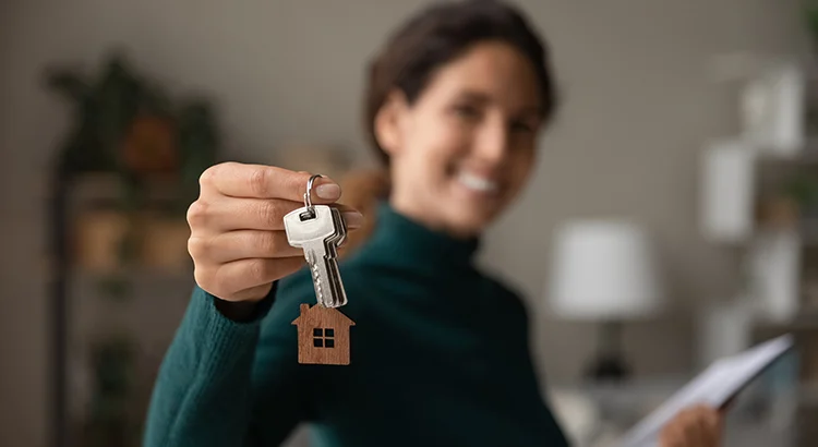 A smiling woman holding house keys with a wooden house keychain