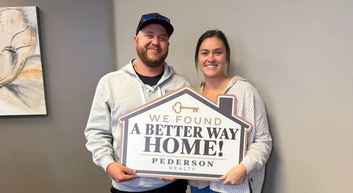 Smiling Pederson Realty buyers holding a We Found A Better Way Home sign