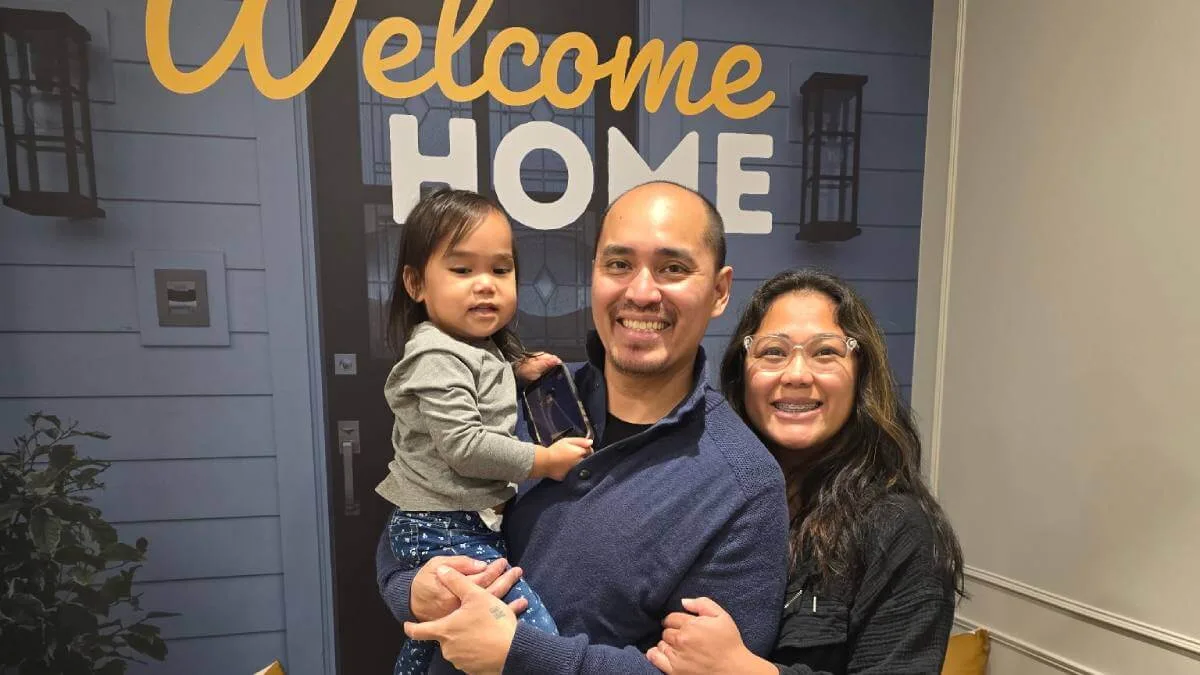 Pederson Realty buyers holding their daughter beneath a Welcome Home sign