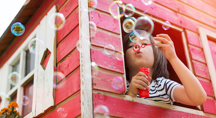 Child blowing bubbles from the window of a pink playhouse