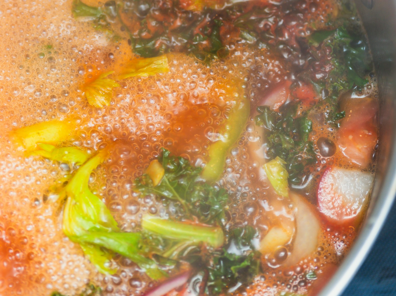 Vegetable soup simmering in a pot with kale and celery