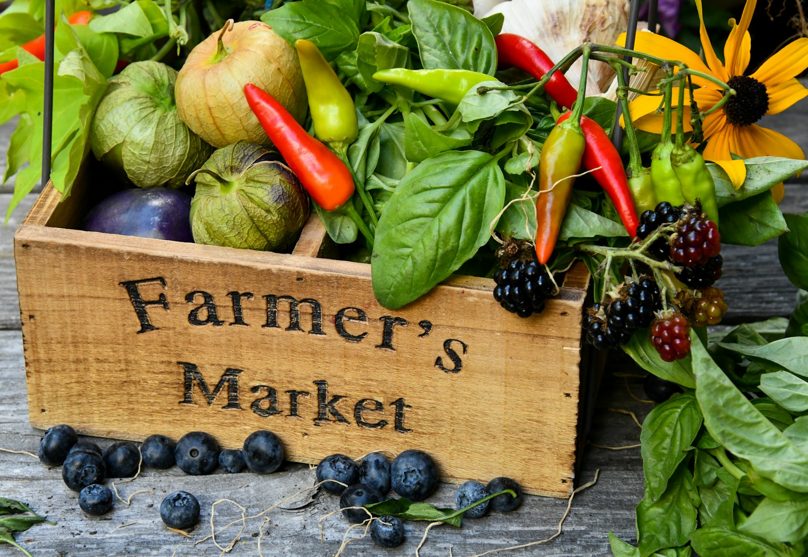 A wooden Farmer's Market crate filled with fresh vegetables, herbs and berries